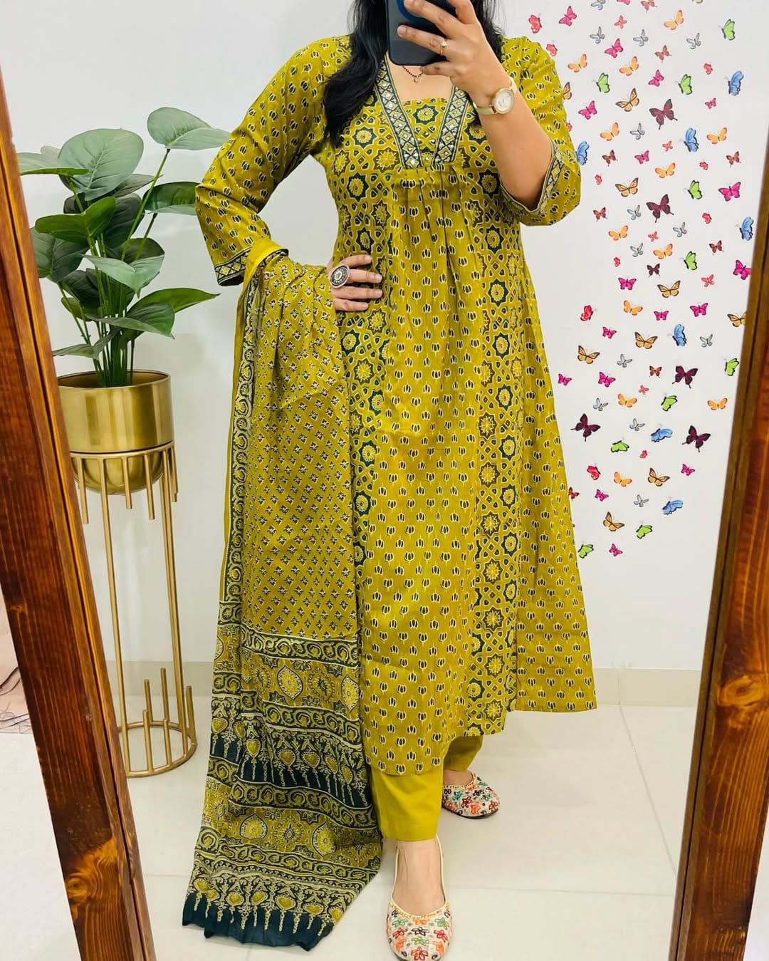 Person wearing a yellow patterned outfit in front of a decorative wall with butterflies.