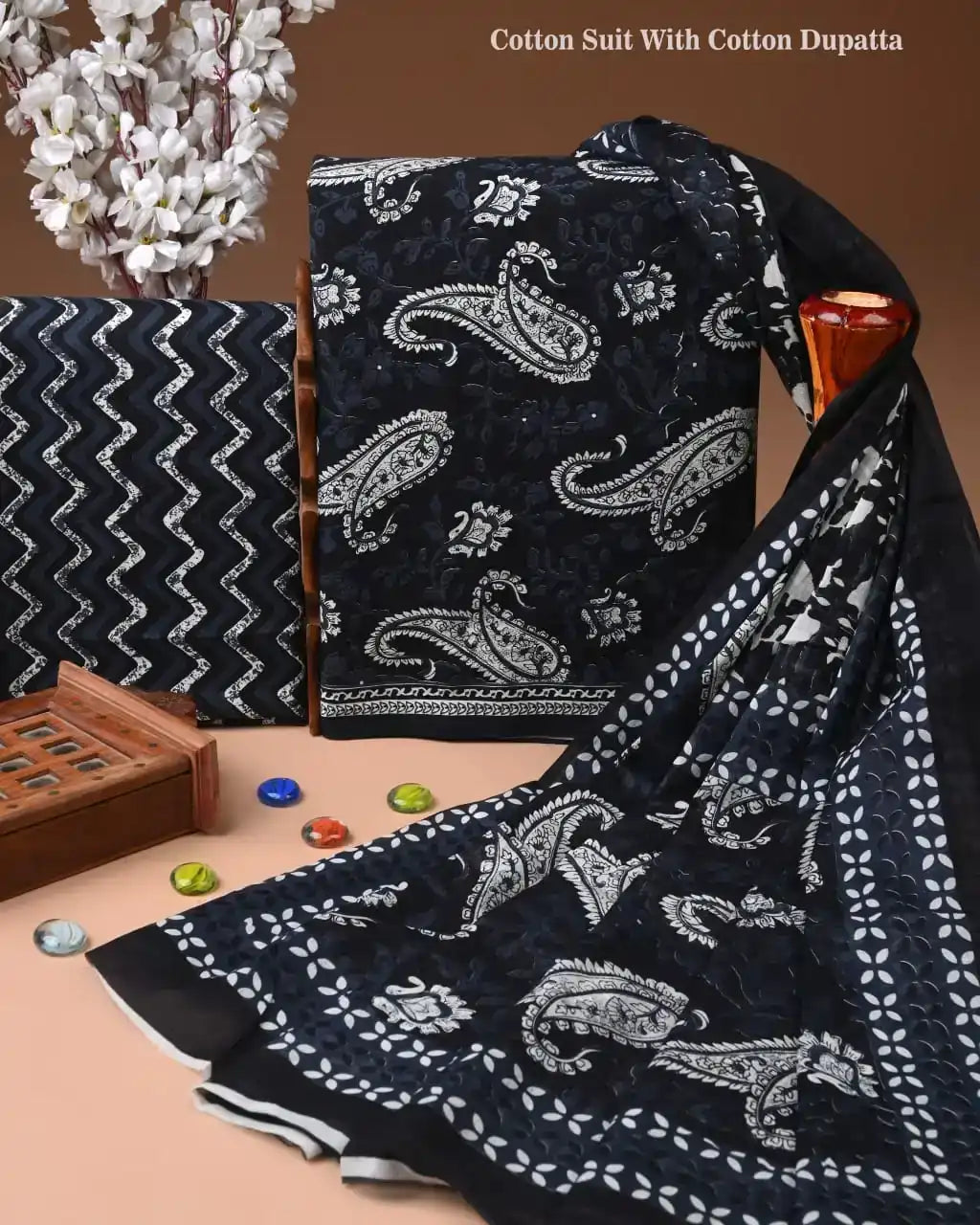 Black cotton suit with white paisley pattern and matching dupatta on a brown background.
