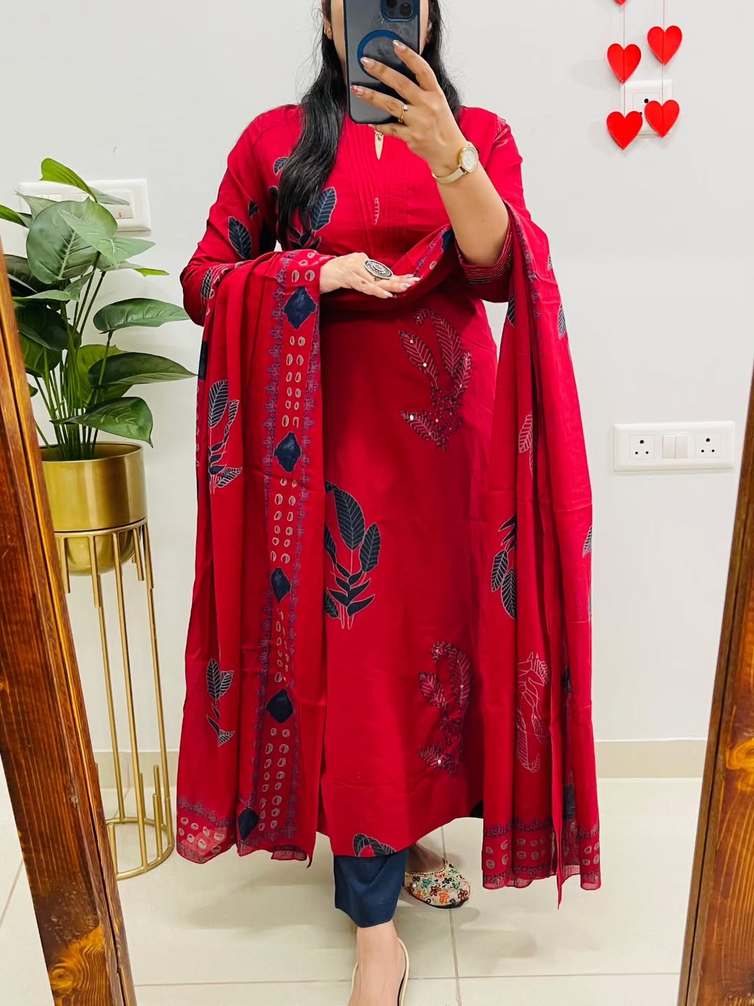 Person wearing a red embroidered outfit with a matching dupatta, standing in front of a mirror.