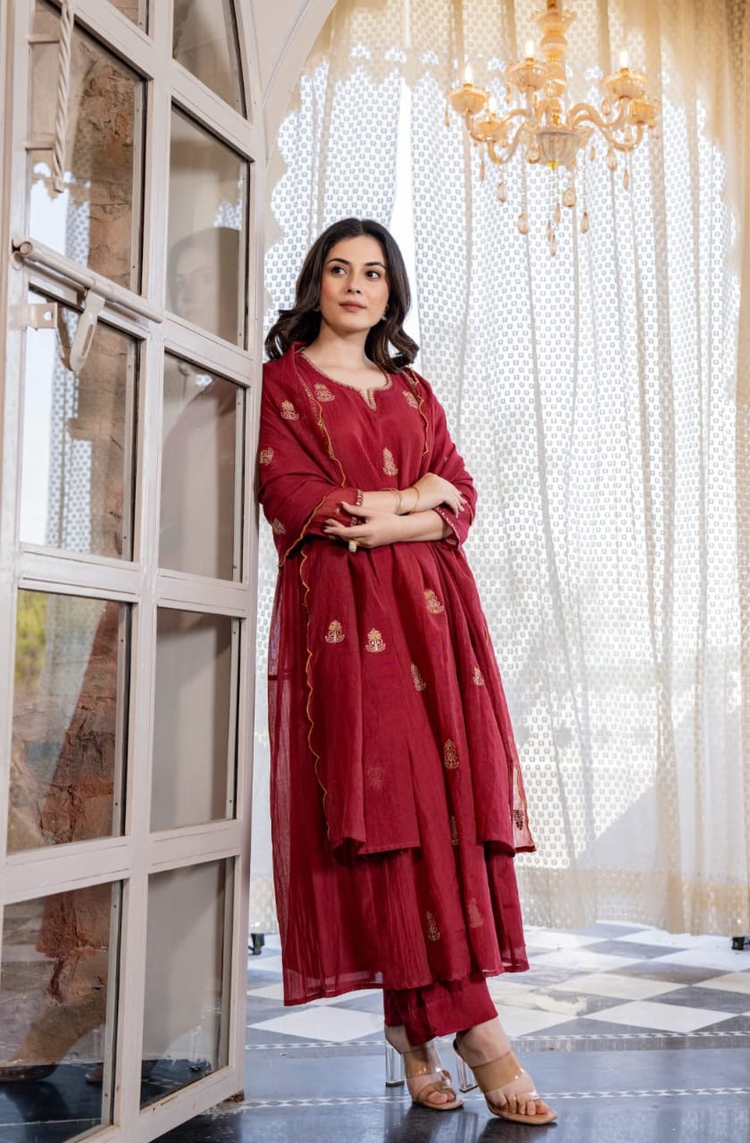 Woman in a red traditional outfit standing in a room with large windows and a chandelier.